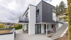 Een modern huis met twee verdiepingen, een balkon, een trap en een terras.