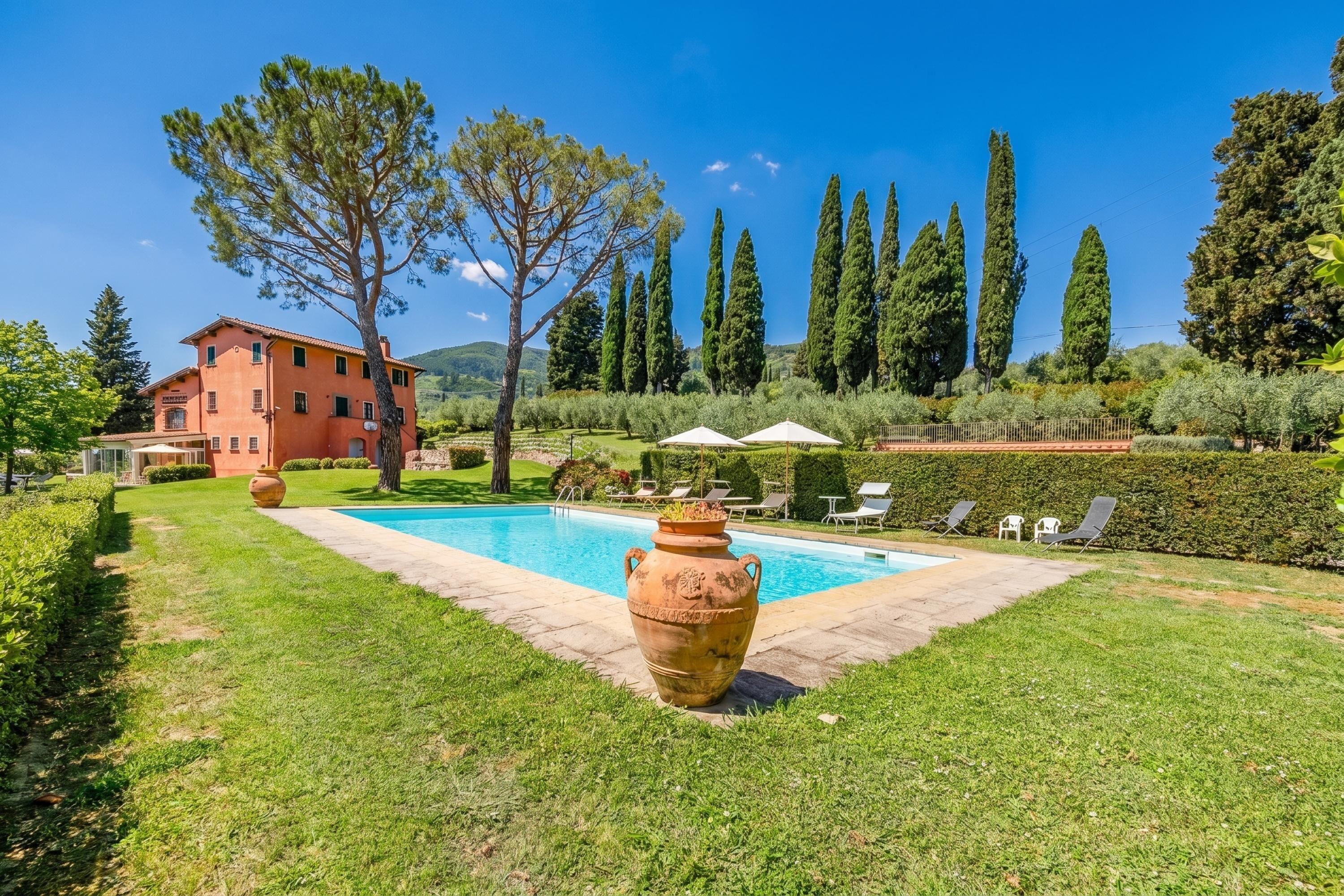 Eine Villa mit Swimmingpool, einem großen Terrakottatopf und einem gepflegten Garten.