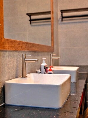 Un baño con un lavamanos rectangular, un espejo y artículos de aseo.