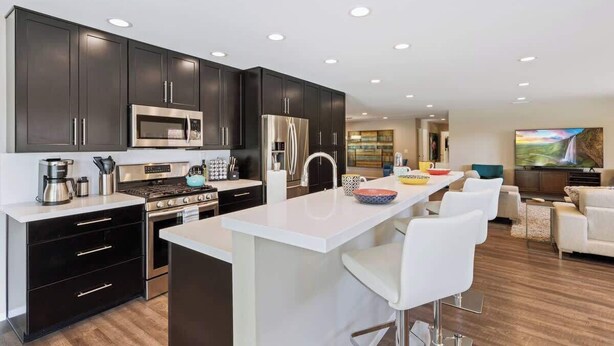 A modern kitchen with dark cabinets, stainless steel appliances, and a bar area with white bar stools. - Sunrise Superstar: Awesome Backyard, Huge Fire Pit (Palm Springs)