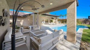 An outdoor patio with a pool, white furniture, and a ceiling fan. - Sunrise Superstar: Awesome Backyard, Huge Fire Pit (Palm Springs)