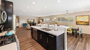 A modern kitchen with a central island, a dining area with a table and chairs, and a living room with a sofa and a TV. - Sunrise Superstar: Awesome Backyard, Huge Fire Pit (Palm Springs)