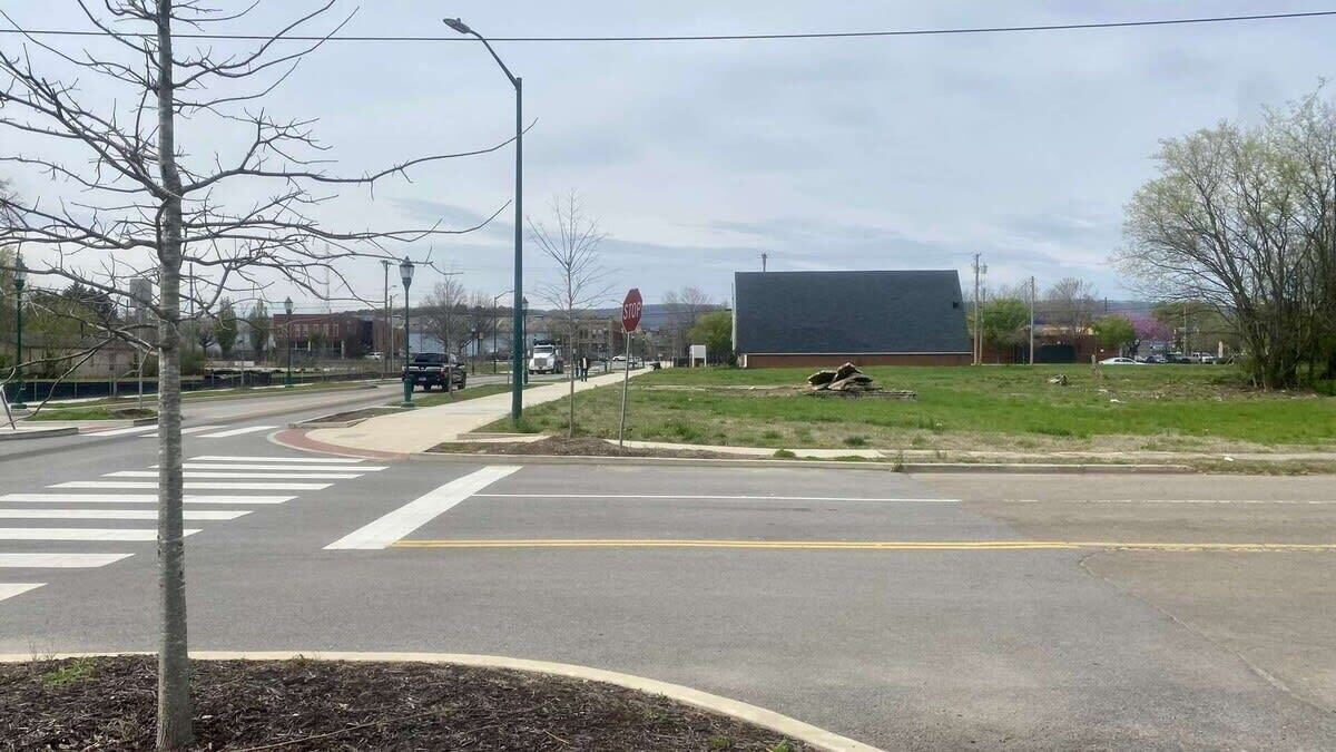 A road intersection with a stop sign, a pedestrian crossing, and a grassy area with a building in the background.