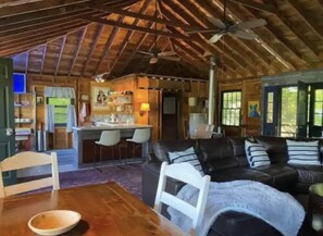 A cozy cabin interior with a dining area, a living room with a sofa and chairs, a kitchen area, and a large window providing natural light. - Airstream Glamping in The Adirondack Foothills (Argyle)