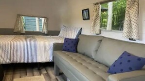 A bedroom with a bed, a sofa, a window with curtains, and a small rug. - Airstream Glamping in The Adirondack Foothills (Argyle)