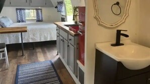 A compact bedroom with a bed, a small table, and a window with curtains. - Airstream Glamping in The Adirondack Foothills (Argyle)