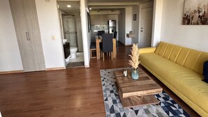 Un salon moderne avec un canapé jaune, une table basse en bois et un coin repas à l’arrière-plan.