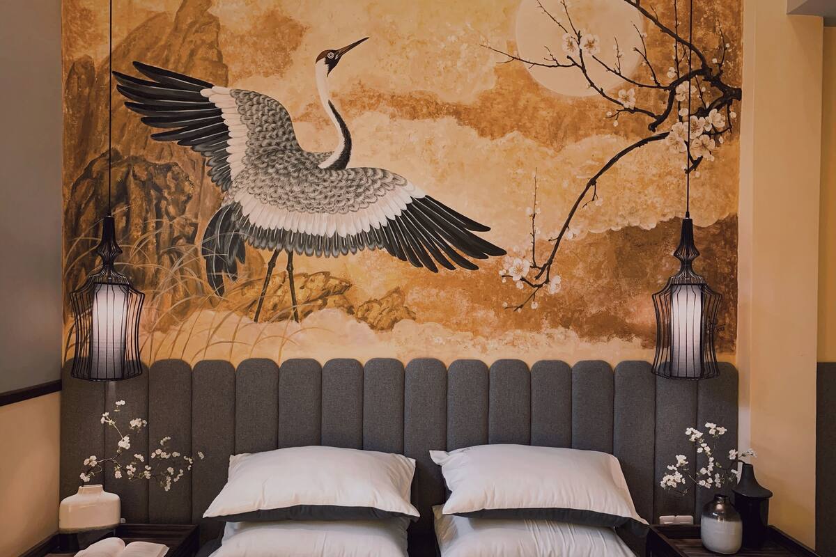 A bedroom with a large bed, two bedside tables, and a wall mural of a crane.