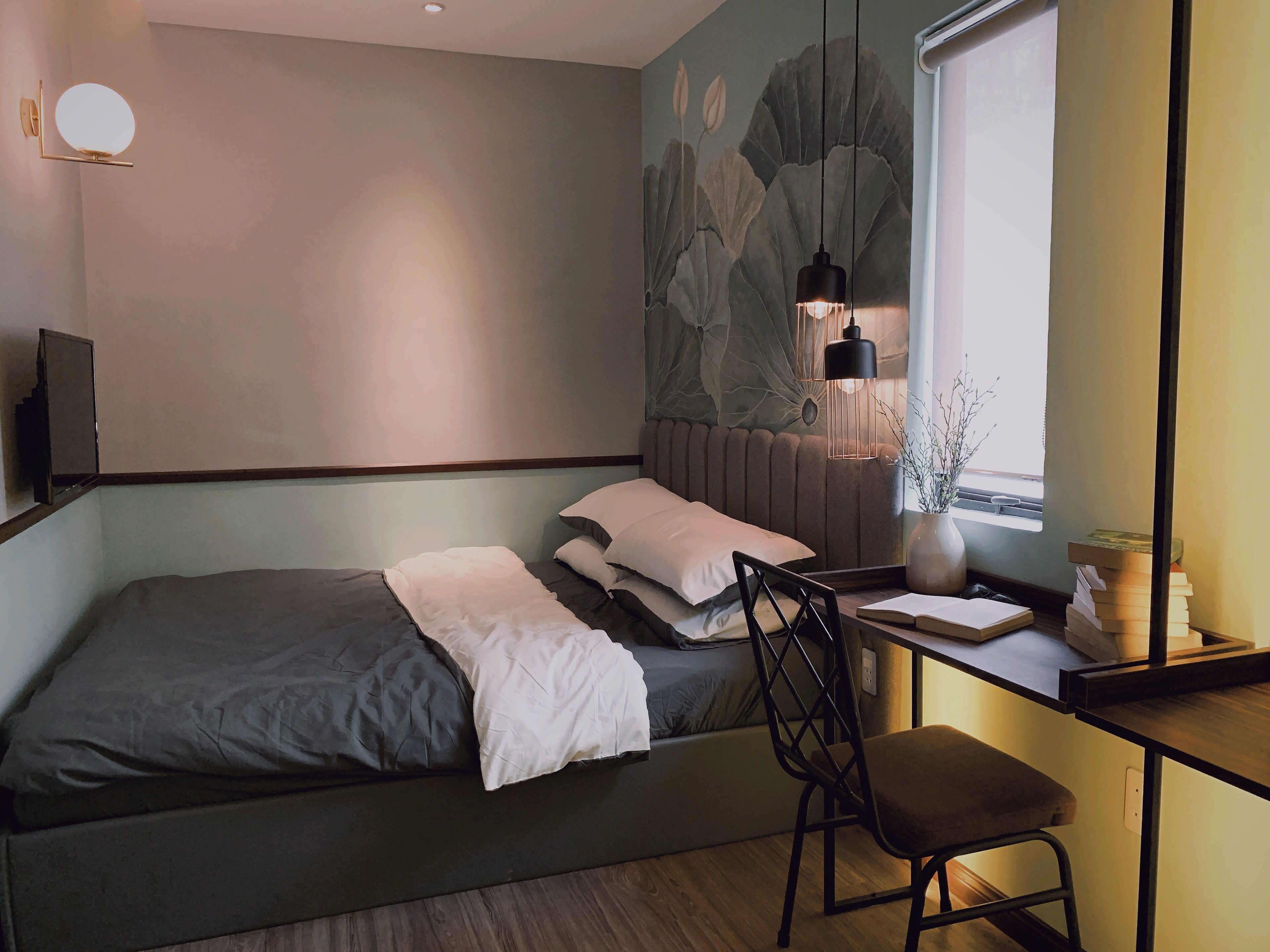 A bedroom with a bed, a desk with a chair, a window, and a wall-mounted mirror.