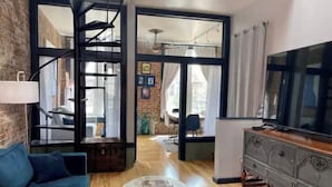 Un salon avec un canapé bleu, une table basse, un téléviseur et un escalier menant à une autre pièce.