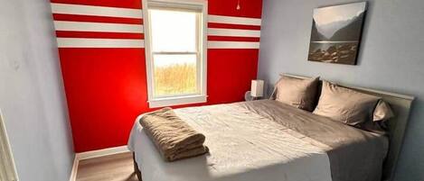 A bedroom with a bed, a ceiling fan, a window, and a wall with red and white stripes.