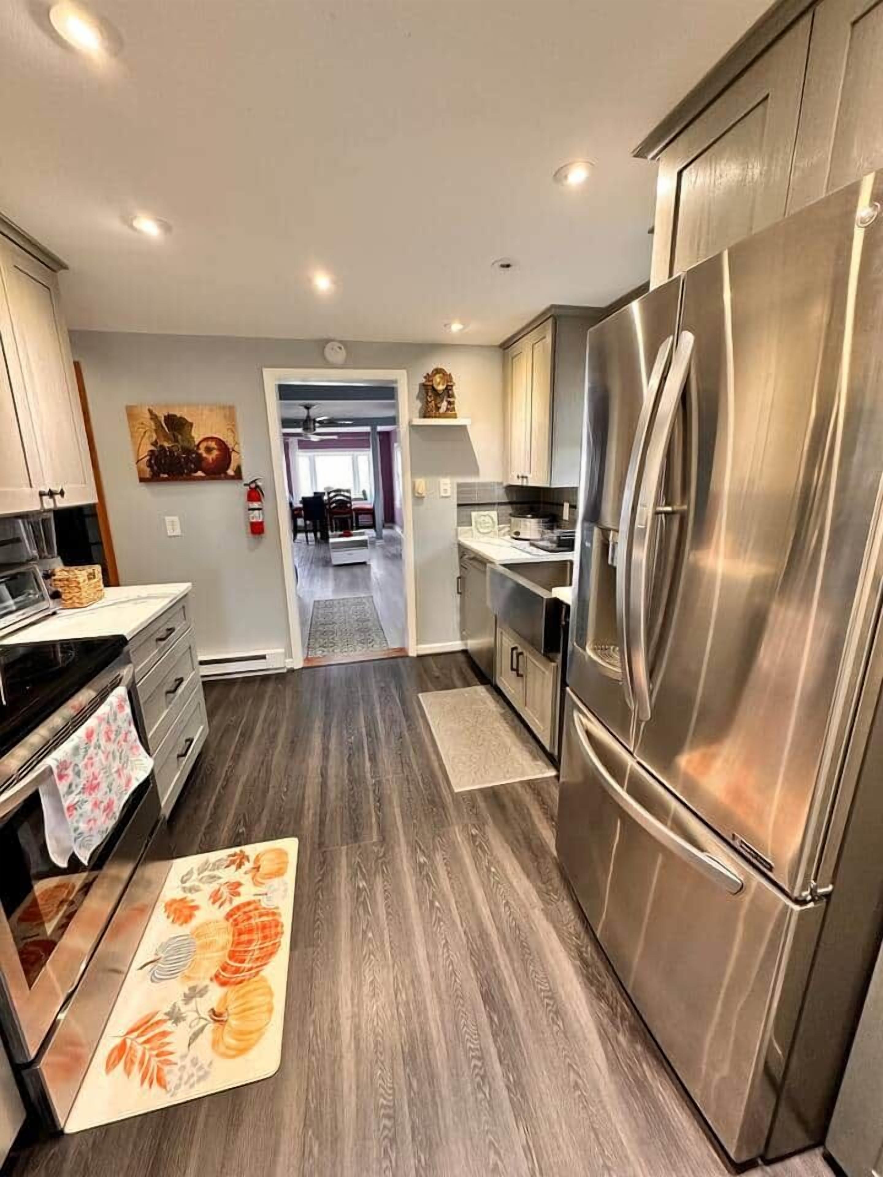 A modern kitchen with stainless steel appliances, wooden flooring, and a view into the dining area.