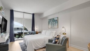 A modern bedroom with a large bed, a desk, a chair, and a balcony with curtains. - Stylish 1BR Condo Rooftop Pool Close to Beach (Boynton Beach)