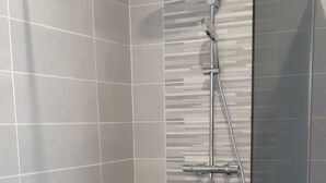 Une salle de bain moderne avec une douche à l’italienne en verre, des murs recouverts de carreaux gris et un sol noir.