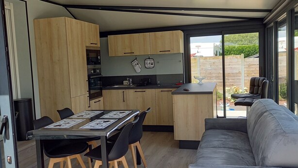 Une cuisine moderne avec des meubles en bois, une table à manger avec des chaises et un canapé gris.
