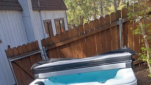 A hot tub with a wooden deck and a metal step, surrounded by a wooden fence and a house in the background. - Charming & cozy cabin (Big Bear)