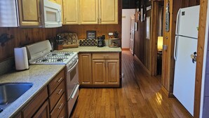 A kitchen with wooden cabinets, a gas stove, a microwave, and a refrigerator. - Charming & cozy cabin (Big Bear)