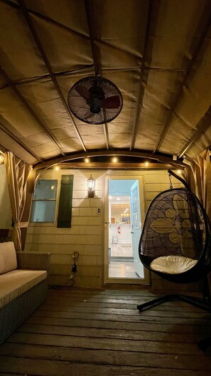 A cozy interior with a wooden floor, a wicker sofa, a hanging chair, and a ceiling fan.