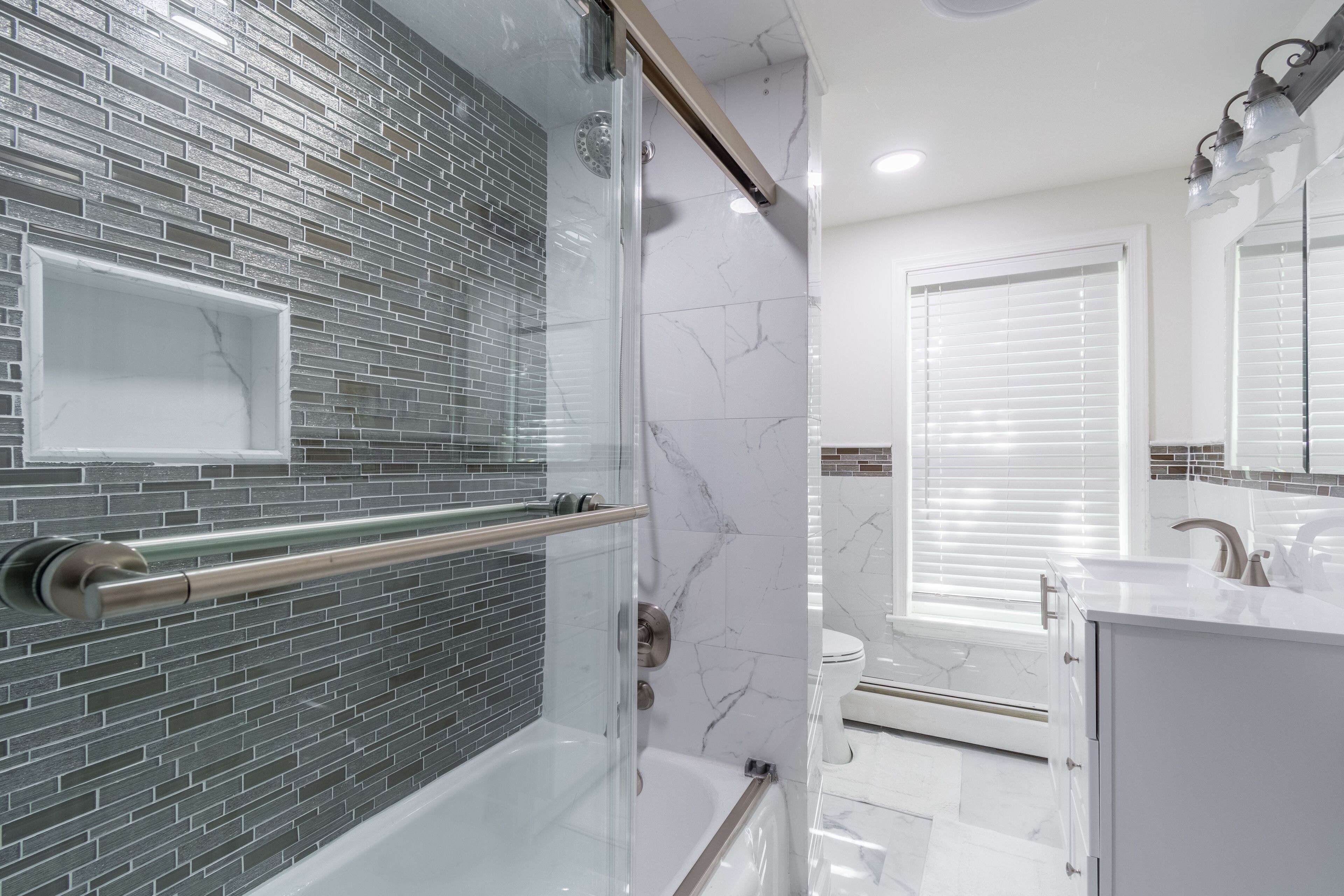 Une salle de bain moderne avec une douche à parois de verre, une baignoire blanche et un lavabo blanc avec un miroir au-dessus.