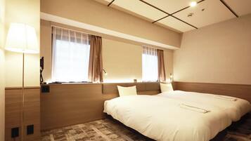 A hotel room with a large bed, a bedside table with a lamp, a window with curtains, and a wall-mounted phone.