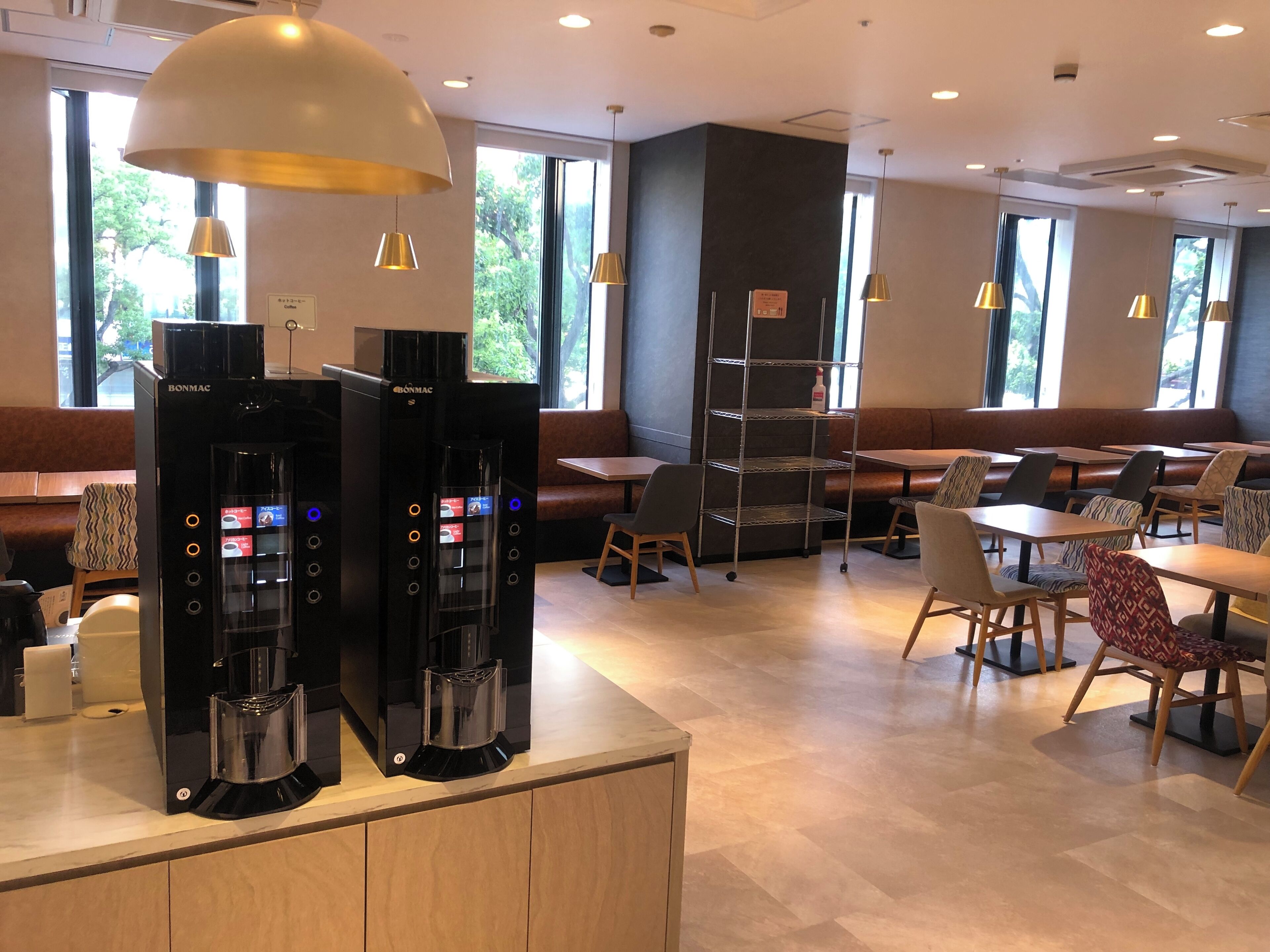 Un café moderno con dos máquinas de café, zonas de estar y ventanas amplias.