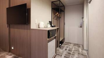Habitación de hotel compacta con televisión de pantalla plana, minibar, refrigerador pequeño, cafetera y perchero.