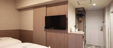 A hotel room with two beds, a TV mounted on a wooden cabinet, a small desk with a mirror, and a door leading to a bathroom.