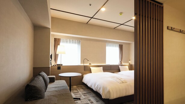 A modern hotel room with a large bed, a sofa, a small round table, and a mirror. - SK HOTEL KOBE STATION FRONT (Kobe)