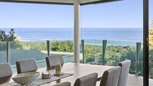 Uma sala de jantar com vista para o oceano e vegetação.