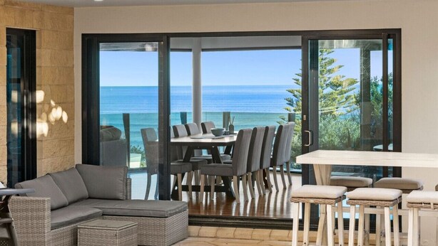 Uma sala de jantar moderna com uma mesa grande e cadeiras, um sofá, e vista para o oceano.
