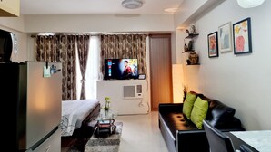 A modern living room with a flat-screen TV, a sofa, a coffee table, and a bed. - One Palm Tree Villas - Unit 3i and 3j (Pasay)