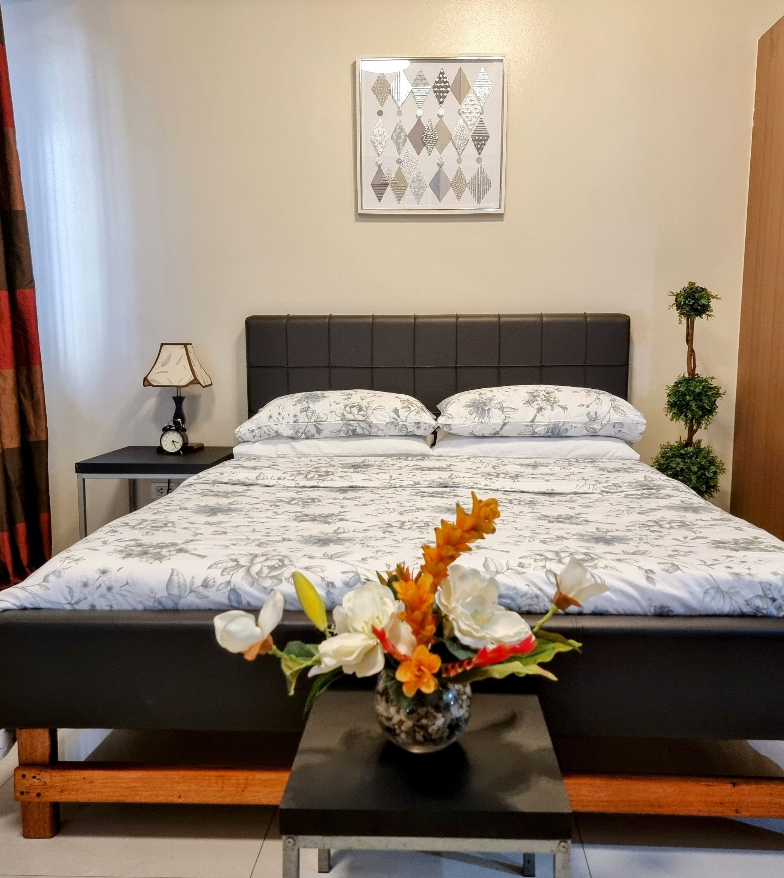 A neatly made bed with floral bedding, a bedside table with a lamp, and a small decorative plant.