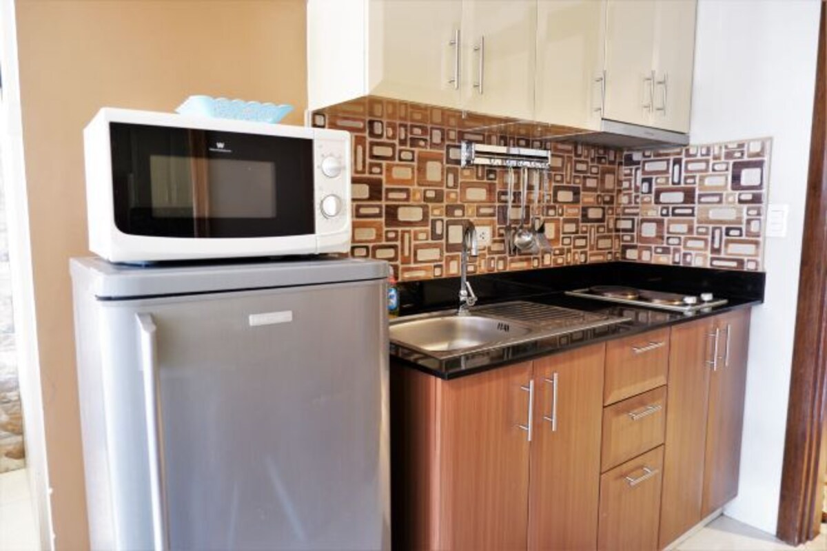 A compact kitchen with a microwave on top of a refrigerator, a sink, and wooden cabinets.