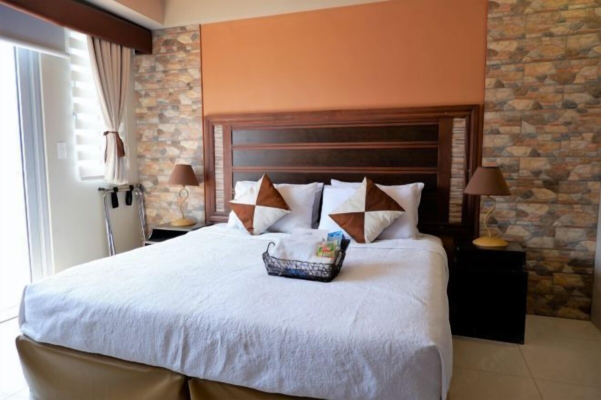 A hotel room with a large bed, stone wall, wooden headboard, and two bedside lamps.