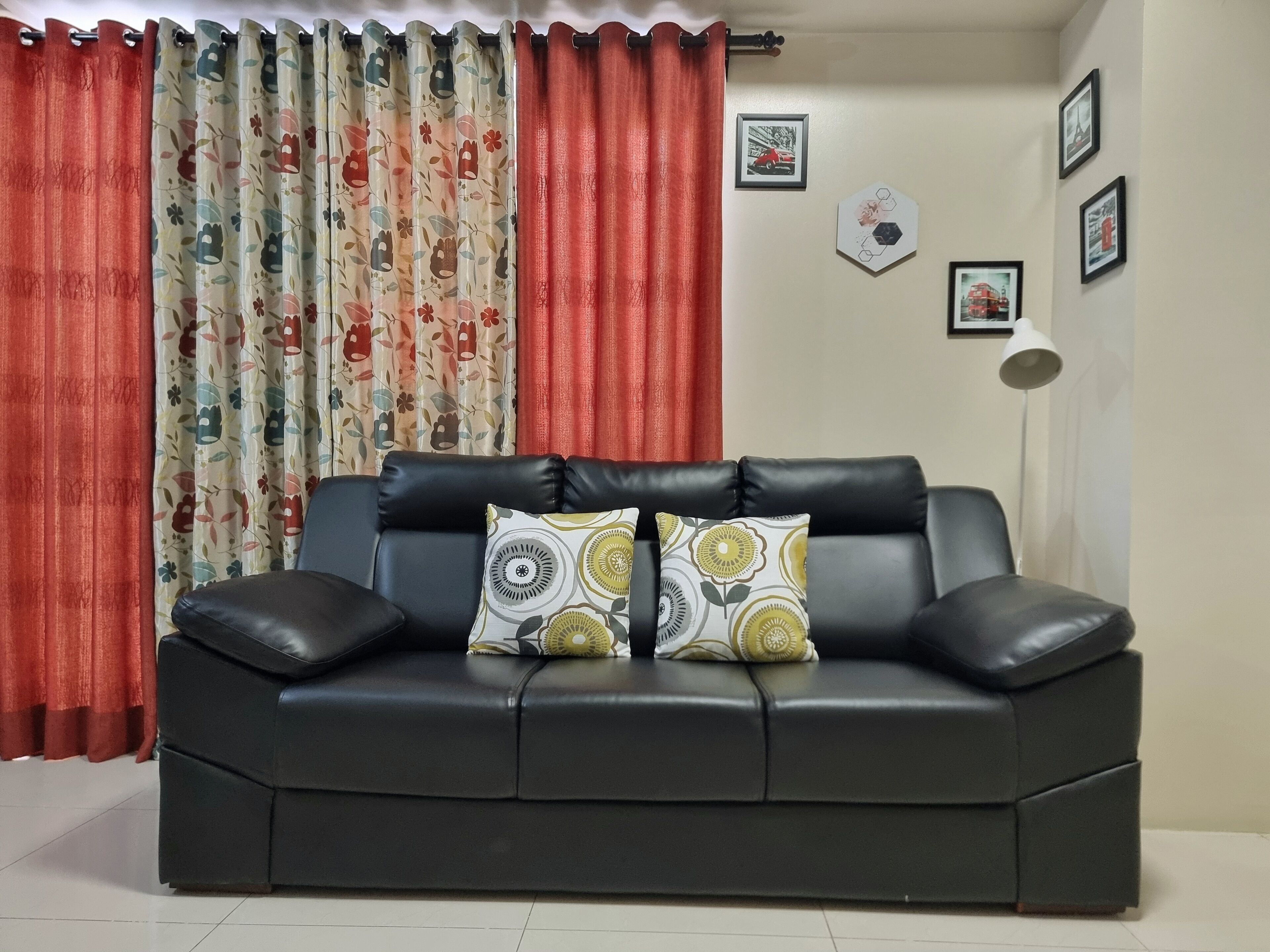 A black leather sofa with two patterned cushions, red curtains, and framed pictures on the wall.