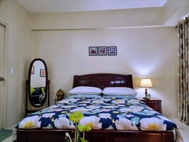 Una cama bien hecha con una colcha estampada, una lámpara de noche y un reloj en la mesita.