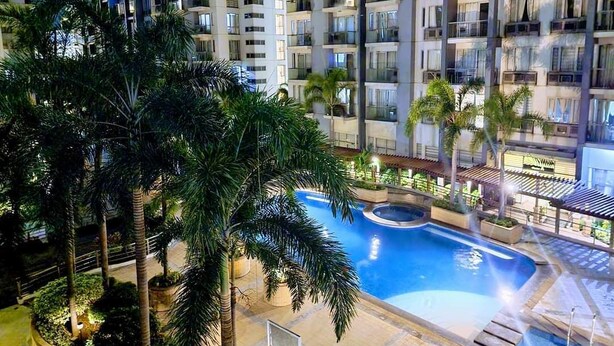 A high-rise residential building with multiple balconies, a swimming pool, and surrounding palm trees. - One Palm Tree Villas - Unit 3i and 3j (Pasay)
