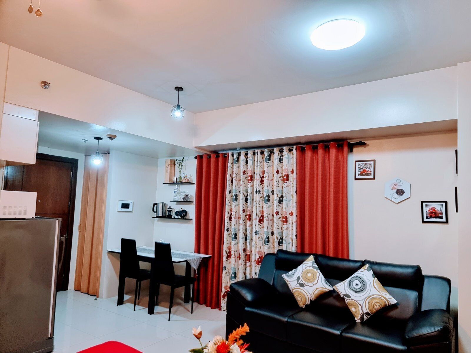 A living room with a black leather sofa, red curtains, and a dining area with a table and chairs.