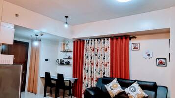 A living room with a black leather sofa, red curtains, and a dining area with a table and chairs.