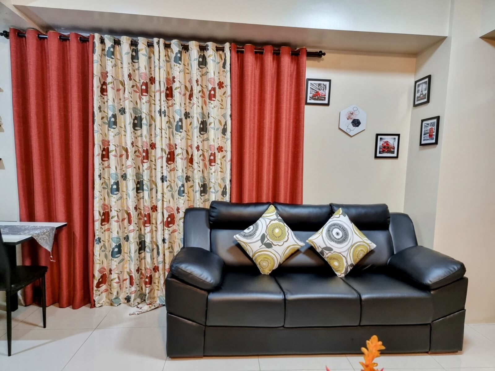 A living room with a black leather sofa, red curtains, and floral patterned curtains.