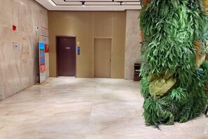 Un vestíbulo de hotel con suelo de mármol, una recepción y una pared decorativa verde.