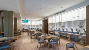 A modern restaurant with wooden flooring, multiple dining tables and chairs, a long counter with a display case, and a television screen. - Xierdun Yixuan Hotel (Lishui)