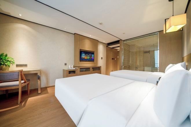 Habitación de hotel moderna con dos camas, un escritorio, una silla, un televisor y un ventanal grande.