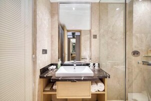 Un baño moderno con un espejo grande, un lavamanos y una cabina de ducha con mampara de vidrio.