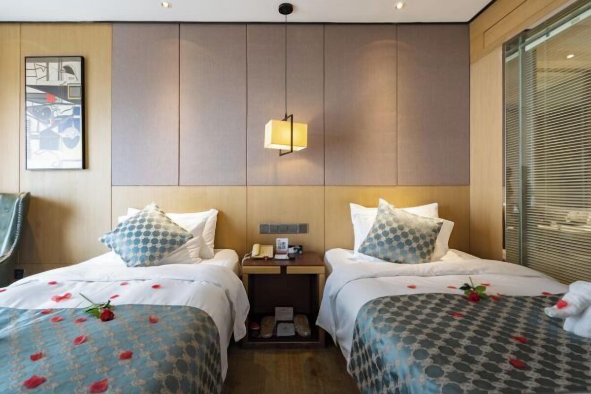 Habitación de hotel con dos camas, una mesita de noche, una lámpara de pared y un cuadro enmarcado.
