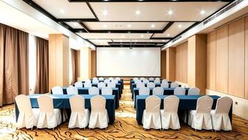 A conference room with rows of tables and chairs, a projector screen, and a patterned carpet.