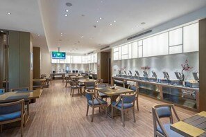 A modern dining area with multiple tables and chairs, a long counter with a display, and a television mounted on the wall. - Xierdun Yixuan Hotel (Lishui)