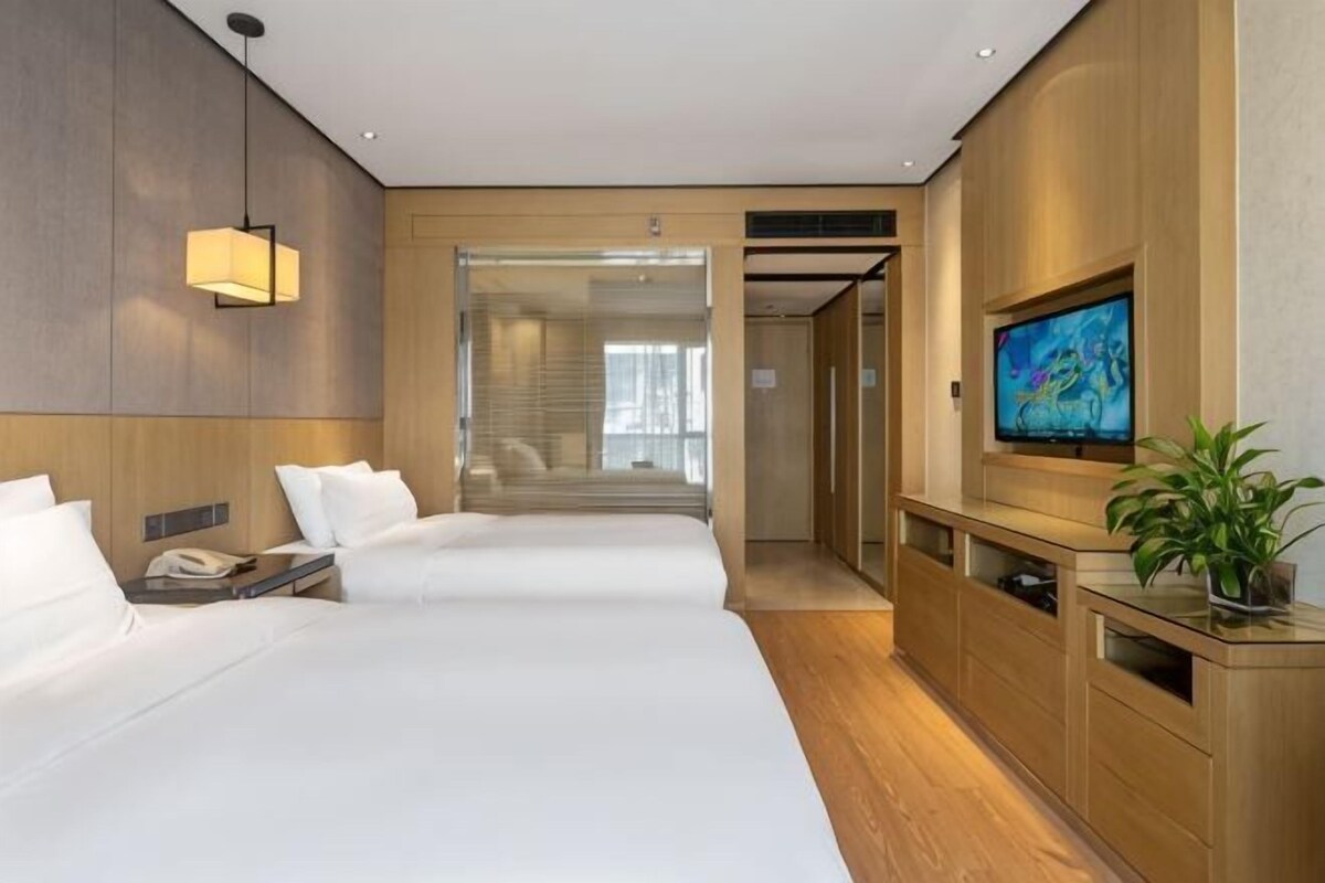 A hotel room with two beds, a TV, a desk, and a plant.