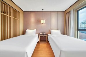 A hotel room with two beds, a wooden floor, a nightstand with a lamp, and a window with a view of buildings. - Xierdun Yixuan Hotel (Lishui)
