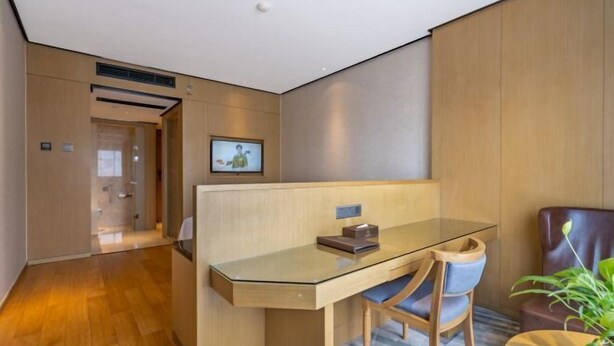 A modern hotel room with a glass desk, two chairs, a small table, a potted plant, and a television on the wall. - Xierdun Yixuan Hotel (Lishui)